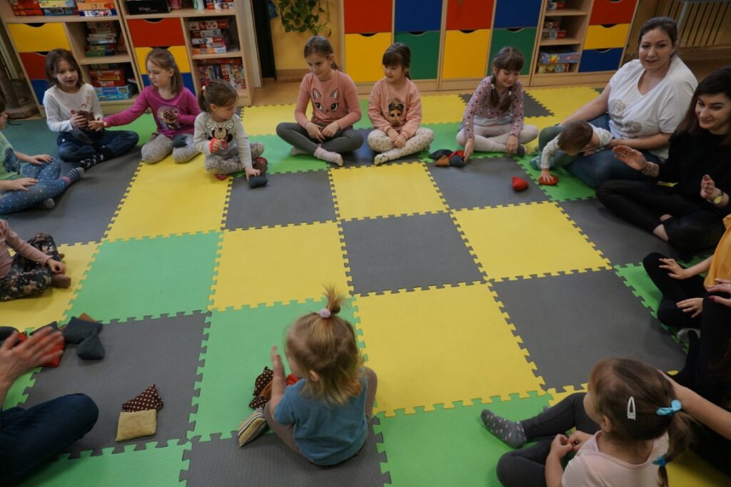 Dzieci i dorośli siedzą w kółeczku i przerzucają woreczki
