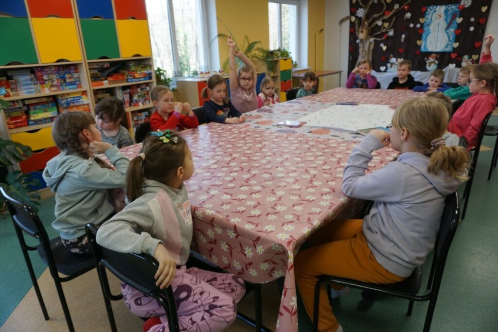 Dzieci siedząc przy stołach odpowiadają na pytania