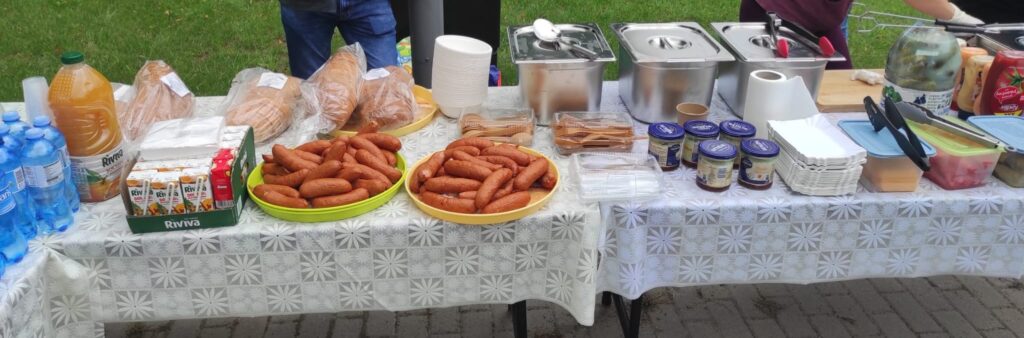 Stół z cateringiem dla rowerzystów, chleb, kiełbasa, napoje, talerzyki papierowe
