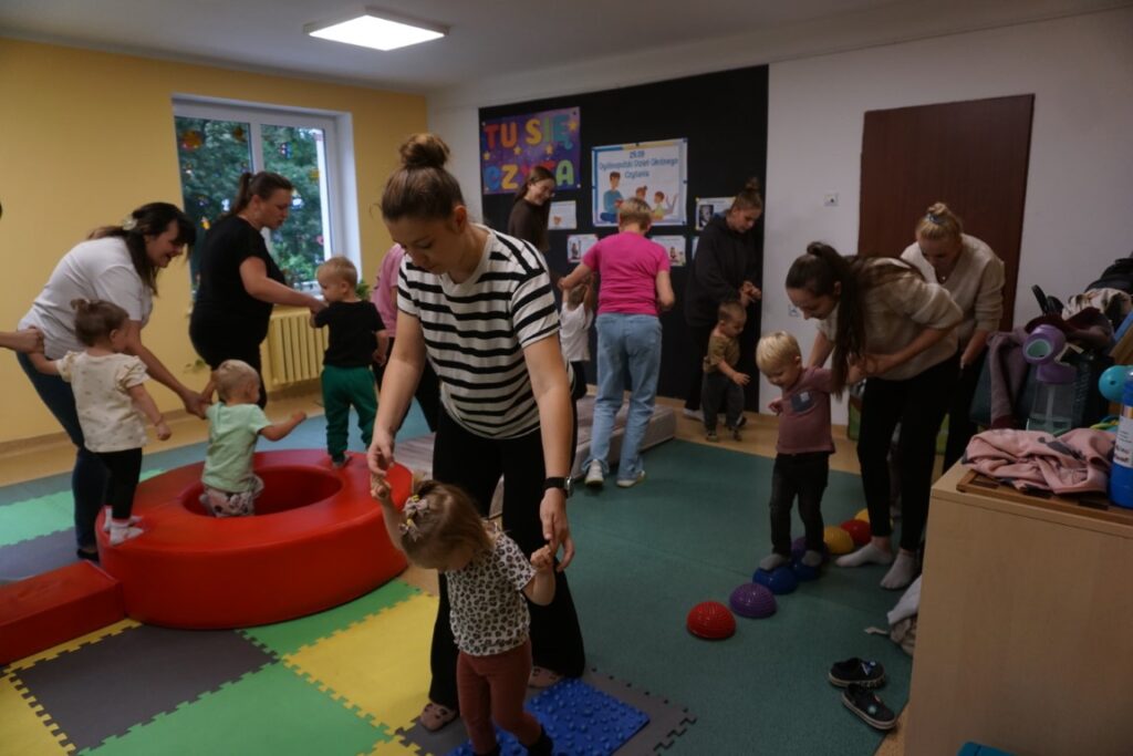 Dzieci z opiekunami chodzą po torze przeszkód,