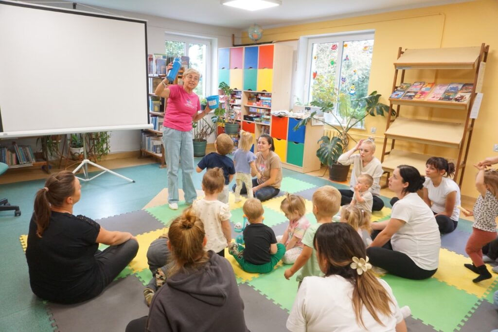 Dzieci, siedzą na macie, słuchają pani bibliotekarki, oddział dla dzieci,