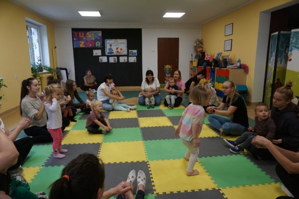 Dzieci, opiekunowie, siedzą na macie,