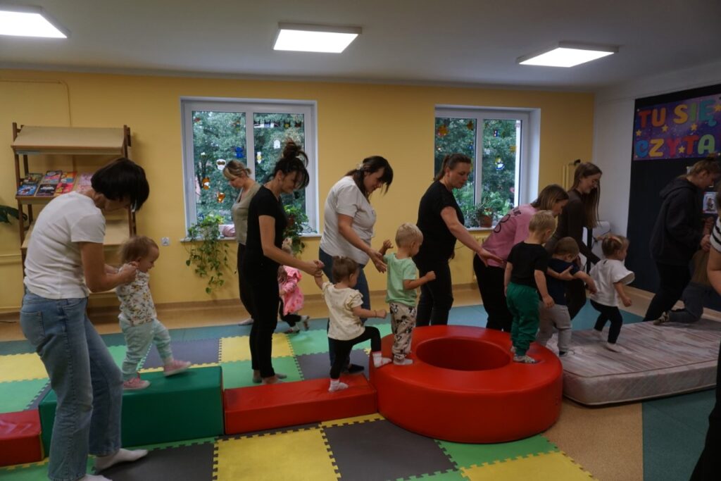 Dzieci z opiekunami chodzą po torze przeszkód,