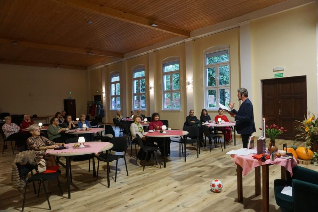 Aktor na tle sceny, publiczność siedząca przy stolikach