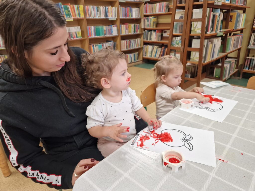 Dzieci z opiekunami malują owoce farbkami przy stoliku