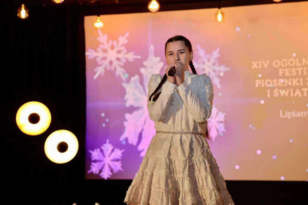 Dziewczynki wokalistki w białych strojach śpiewające na scenie