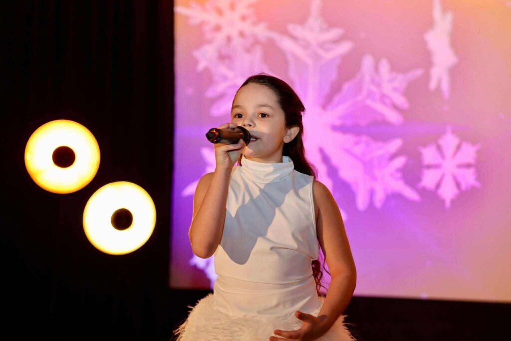 Dziewczynki wokalistki w białych strojach śpiewające na scenie