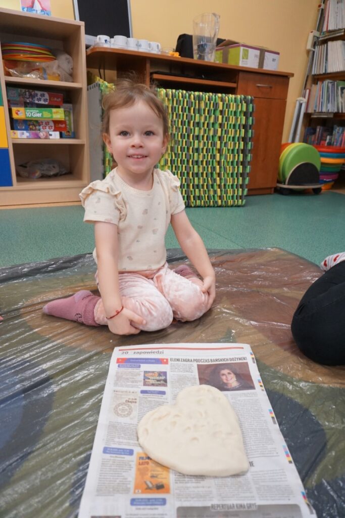 Dziecko siedzące na dywanie, obok serca wykonanego z masy solnej