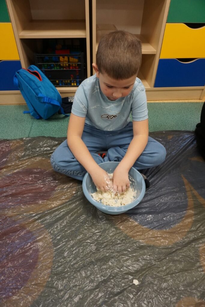 Dziecko siedzące na dywanie, mieszające masę solną w miseczce