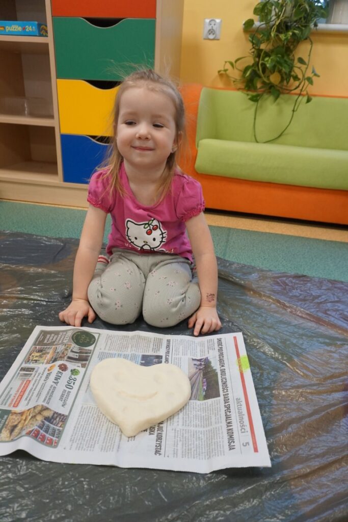 Dziecko siedzące na dywanie, obok serca wykonanego z masy solnej