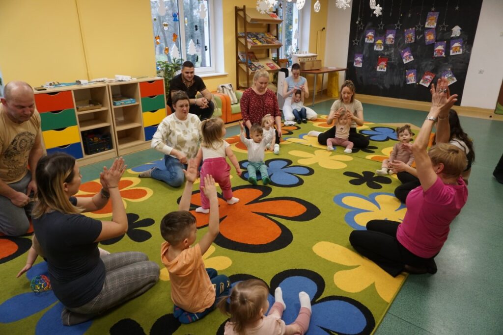 Dzieci z opiekunami siedzący na dywanie i klaszczące