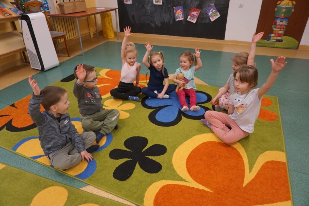 Dzieci siedzące na dywanie i machające do aparatu